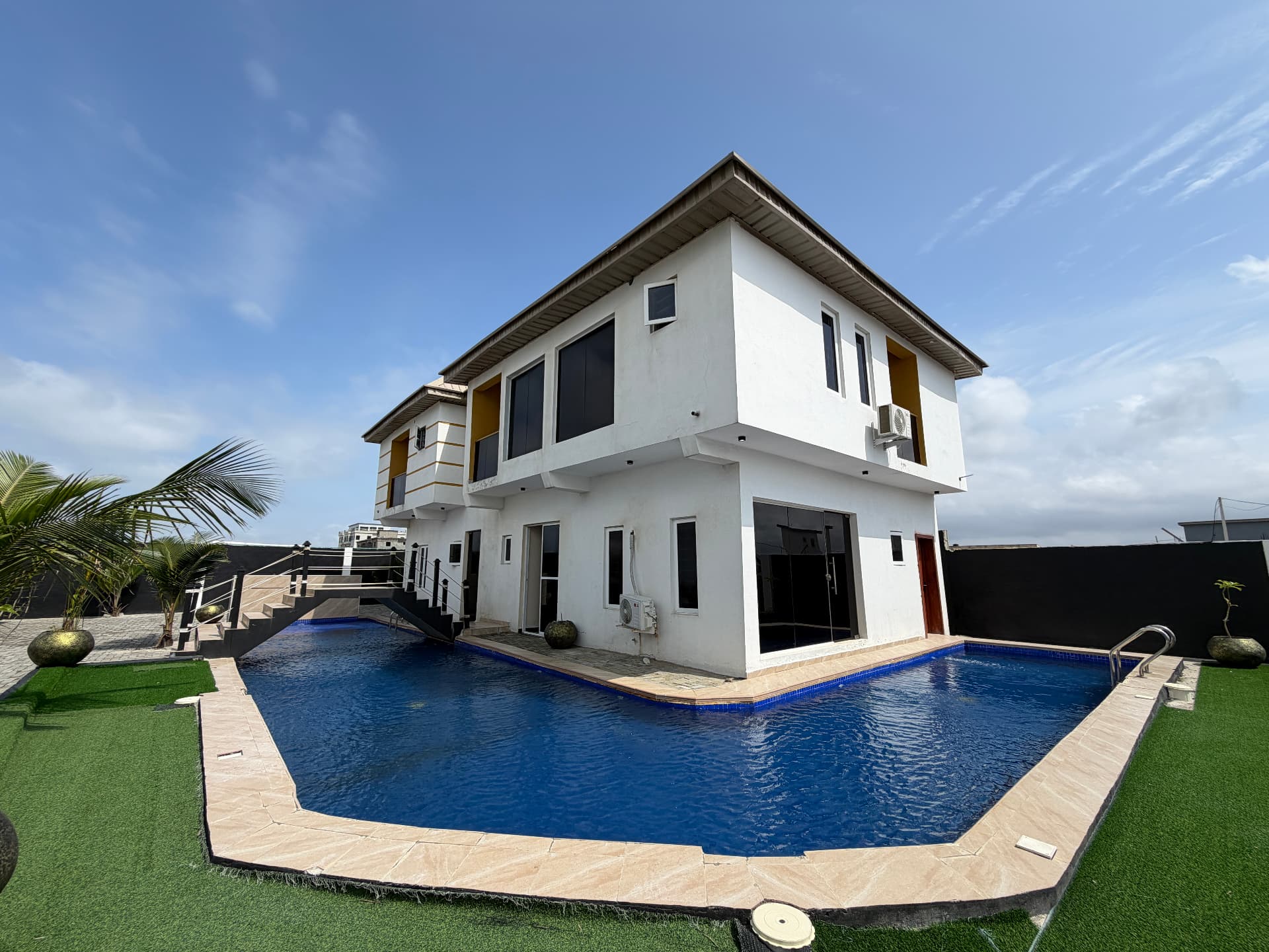 A white two-storey villa at Timeless Haven beside an angular blue swimming pool and lawn